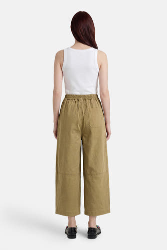 Groene chino broek van ADORE, wijde pasvorm met elastische taille, achterzak en patchdetails, achterzicht model in wit topje en zwarte loafers