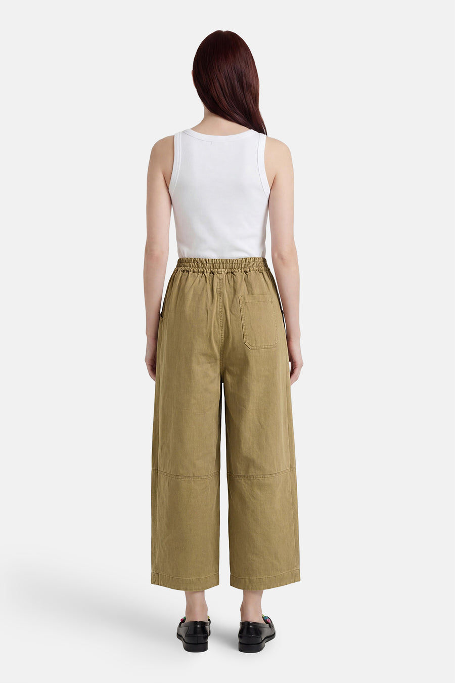 Groene chino broek van ADORE, wijde pasvorm met elastische taille, achterzak en patchdetails, achterzicht model in wit topje en zwarte loafers