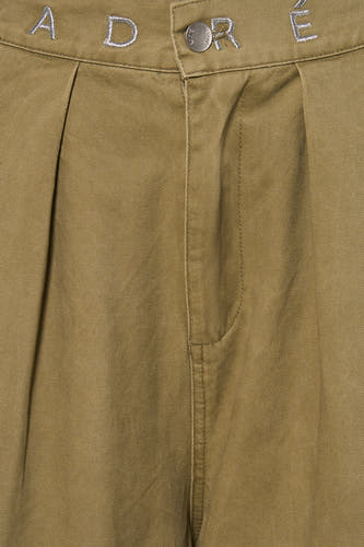 Groene chino broek van ADORE met geborduurd logo en zilveren knoop, close-up van voorkant