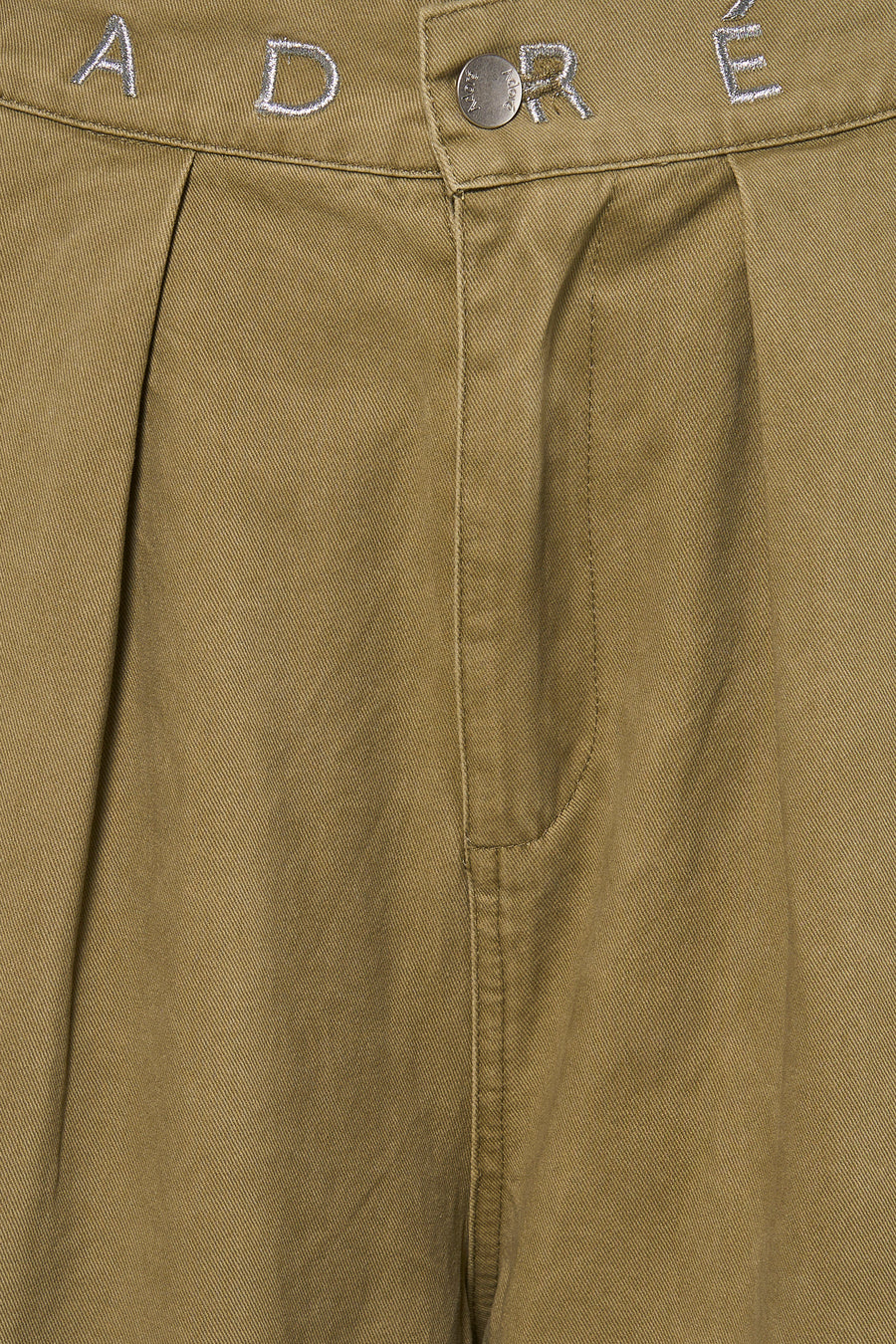 Groene chino broek van ADORE met geborduurd logo en zilveren knoop, close-up van voorkant