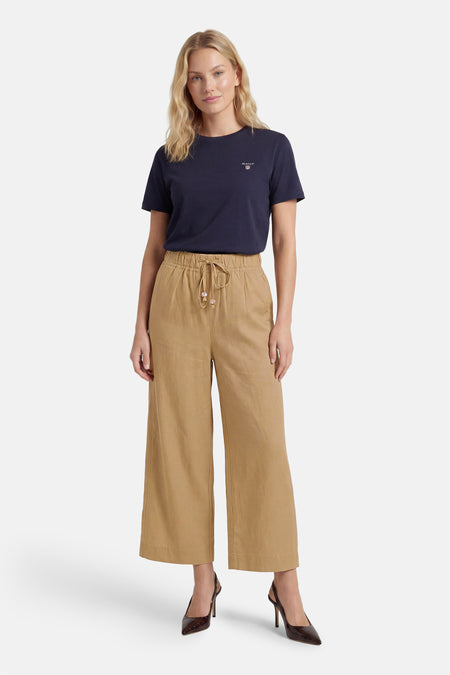 Beige damesbroek met elastische taille van ADORE, wijde pijpen, trekkoord, cropped model, gedragen met donkerblauw T-shirt en bruine hakken
