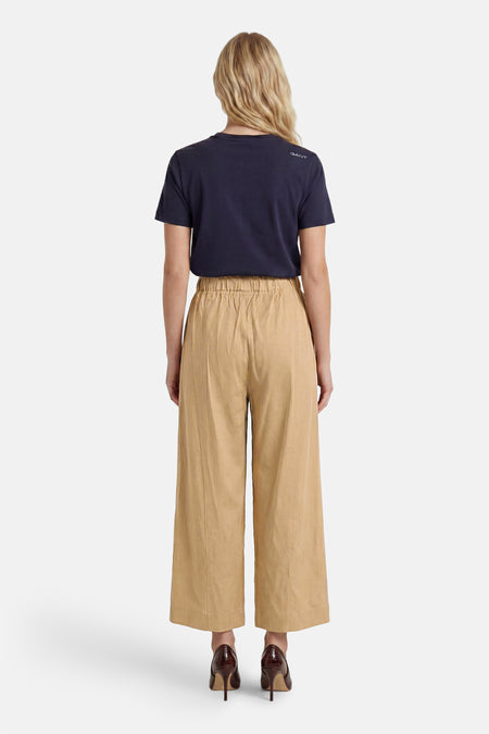Beige damesbroek met elastische taille van ADORE, wijde pijpen, achterkant, model in donkerblauw shirt en bruine hakken