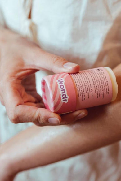 Roze body butter stick van Wondr Care, aangebracht op een arm.

