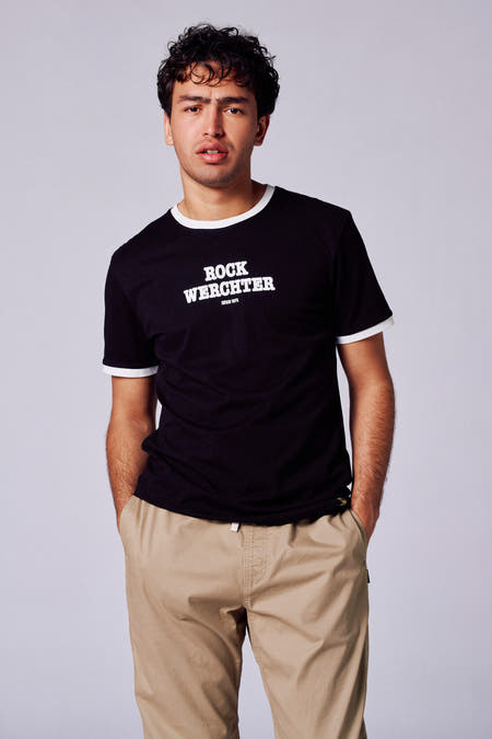 T-shirt noir à manches courtes de Rock Werchter 50, avec une patte blanche le long des manches et du col, associé à un pantalon kaki.