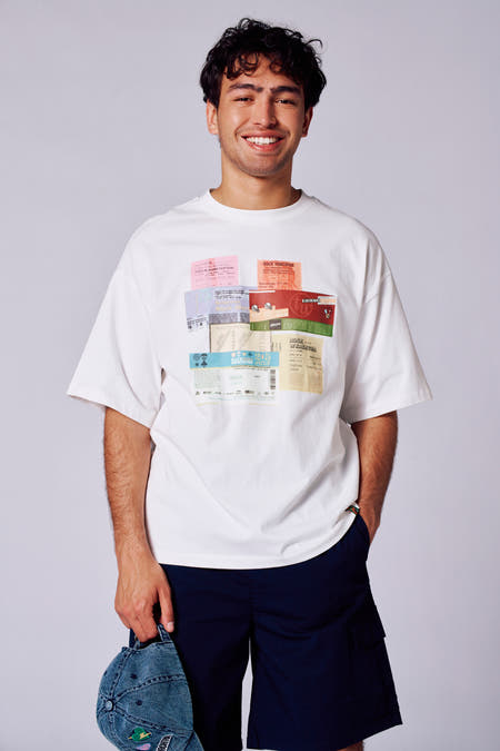 T-shirt blanc à manches courtes de Rock Werchter 50, avec des shorts cargo bleus et une main dans la poche.