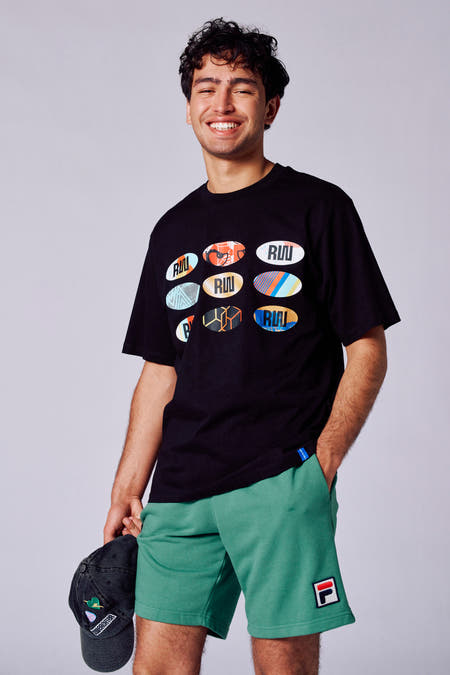 T-shirt noir à manches courtes de Rock Werchter 50, avec neuf badges logo sur l'avant, porté avec des shorts verts.