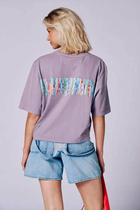 Paars T-shirt met korte mouwen van Rock Werchter 50, met een print van festivalbandjes op de rug, gedragen met een denim short.
