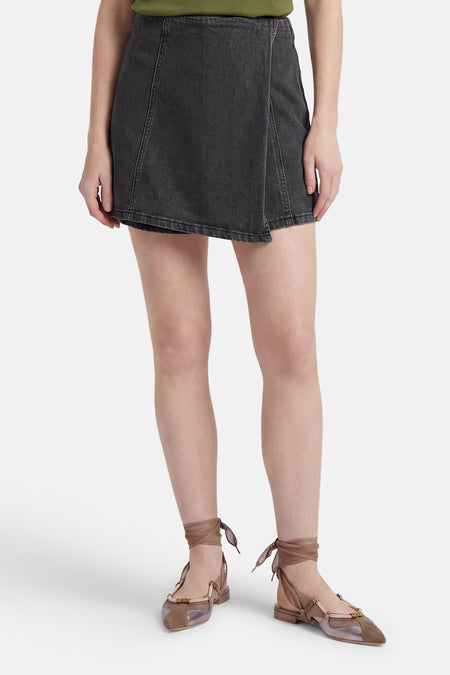 Zwarte denim skort van HAILYS met overslag, zichtbare naden, gecombineerd met een groene top en veterschoenen.