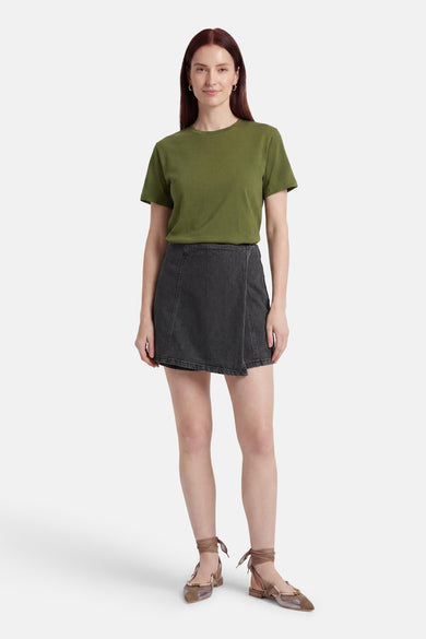 Zwarte denim skort van HAILYS met crossover detail, gedragen door een model met een groen T-shirt en platte schoenen.