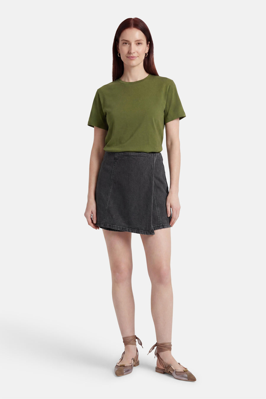 Zwarte denim skort van HAILYS met crossover detail, gedragen door een model met een groen T-shirt en platte schoenen.