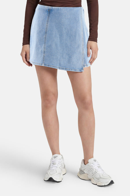 Lichtblauwe denim skort van HAILYS in wikkelrok-stijl met verticale naden, gedragen met een bruine top en witte sneakers.