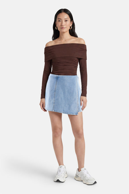 Lichtblauwe denim skort van HAILYS met A-lijn model, gedragen met een bruine off-shoulder top en witte sneakers.
