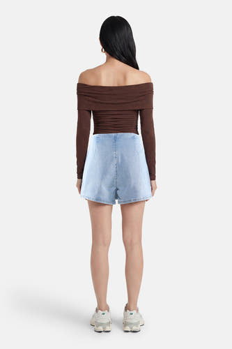 Lichtblauwe denim skort van HAILYS, achterkant, gedragen met een bruine off-shoulder top en witte sneakers.
