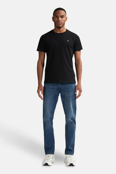 Blauwe tapered jeans van Petrol Industries, gecombineerd met een zwart T-shirt en witte sneakers.