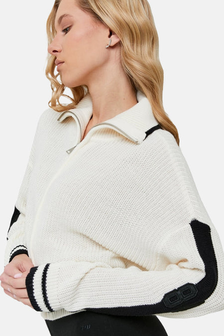 Witte gebreide trui met zwarte details, zilveren rits en blond model.
