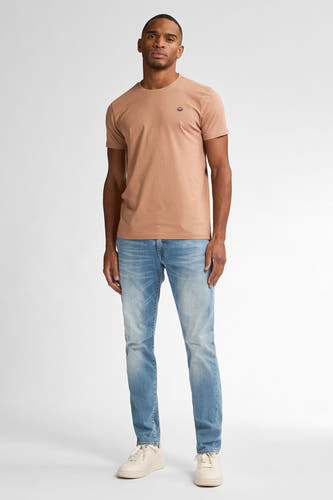 Slim fit jeans van Petrol Industries®, in een lichte wassing, gecombineerd met een bruin T-shirt en crèmekleurige sneakers.
