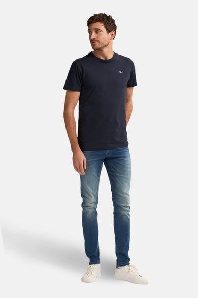 Jean slim fit bleu de Petrol Industries, associé à un T-shirt bleu marine et des baskets blanches.