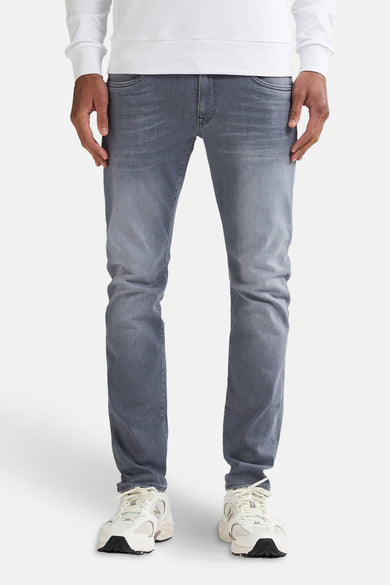 Jean slim en denim gris de Petrol Industries, avec un lavage subtil et porté avec des baskets blanches et un sweat-shirt blanc.