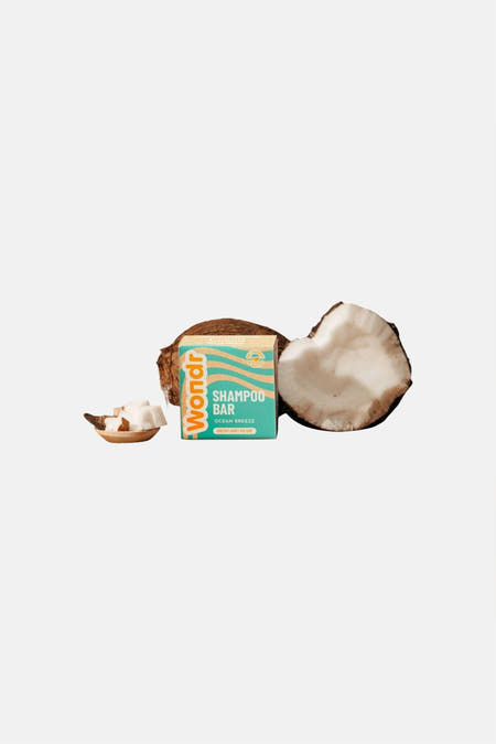 Shampoo bar in een turquoise doos met beige golfpatroon van WONDR CARE, tussen halve kokosnoten en een houten schaaltje met kokosstukjes.