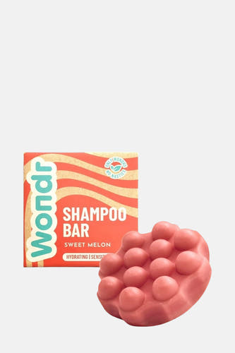 Roze shampoo bar met nopjes van WONDR CARE, naast een productverpakking met oranje en beige strepen.