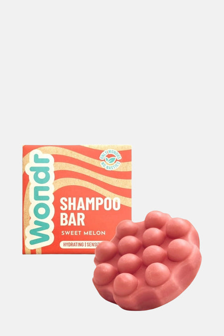 Roze shampoo bar met nopjes van WONDR CARE, naast een productverpakking met oranje en beige strepen.