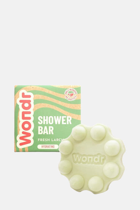 Douche verte de WONDR CARE sur un support vert avec une pierre blanche et une plante en premier plan.