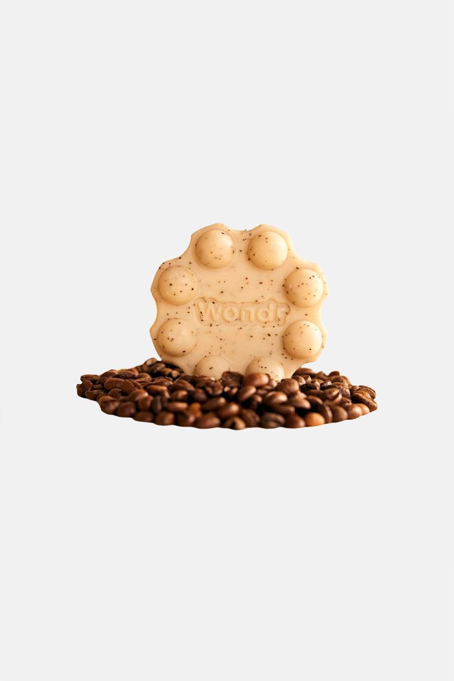 Beige vaste douchegel met spikkels en pop-it design van WONDR CARE, met 'Wondr' reliëf, staand op koffiebonen.