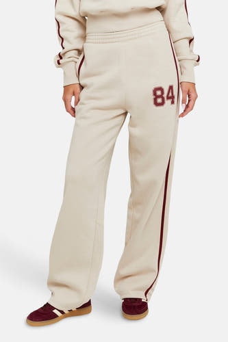 Jean de jogging beige TALLY WEIJL, avec un détail brodé '84' et des rayures bordeaux le long des côtés.