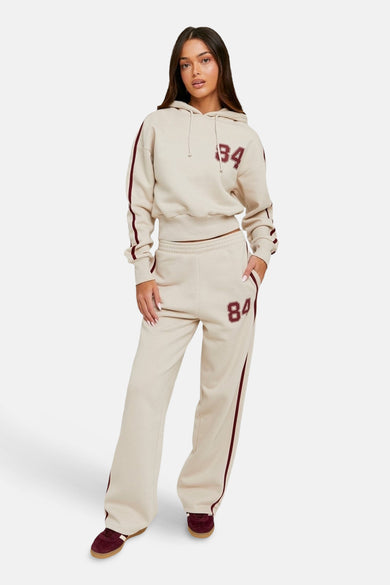 Beige joggingbroek van TALLY WEIJL met bordeauxrode streep en nummer, gecombineerd met bijpassende hoodie en schoenen.
