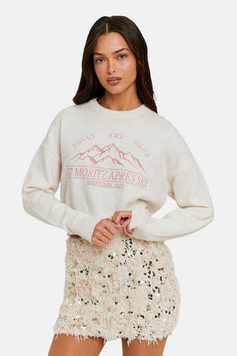 Pull-over blanc avec col rond de TALLY WEIJL, imprimé d'un club de ski rose et porté avec une jupe brillante.