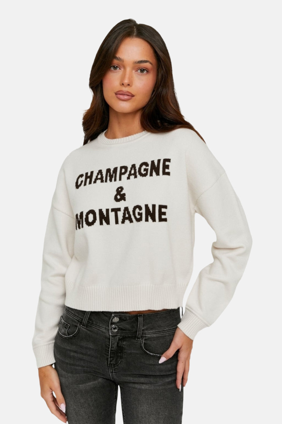 Ecrukleurige trui met ronde hals van TALLY WEIJL, met opschrift 'Champagne & Montagne', gecombineerd met een grijze jeans.
