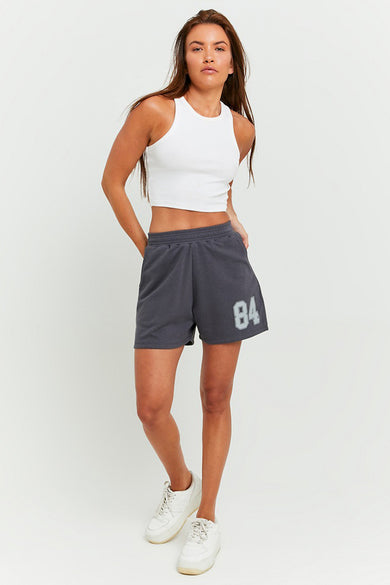 Grijze short van TALLY WEIJL, met het nummer 84, gecombineerd met een witte top en witte sneakers.