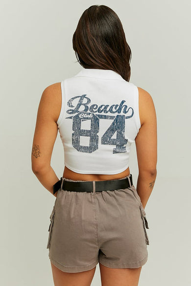 Witte top zonder mouwen van TALLY WEIJL, met 'Beach Club 84' print op de rug, gecombineerd met grijze shorts en een zwarte riem.
