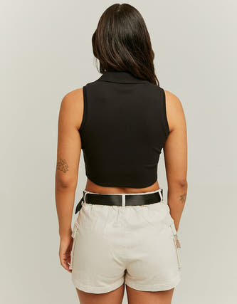 Zwarte mouwloze top van TALLY WEIJL, met een kraag en cropped model, gecombineerd met een beige short met riem.
