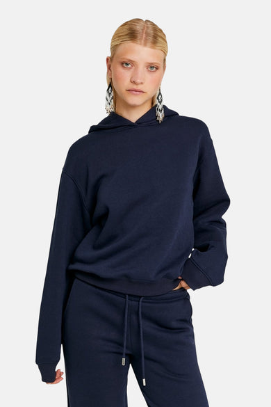 Pull-over bleu avec capuche de TALLY WEIJL, porté avec un pantalon coordonné et des boucles d'oreilles longues.