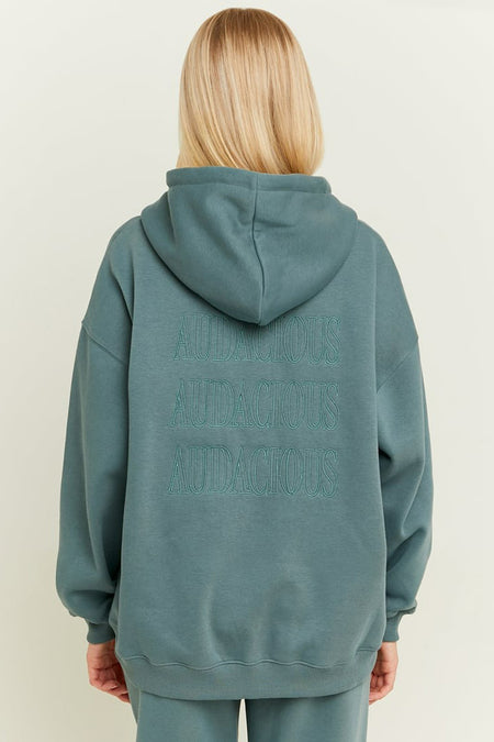 Gilet turquoise de TALLY WEIJL avec capuchon et texte 'Audacious' répété sur le dos.