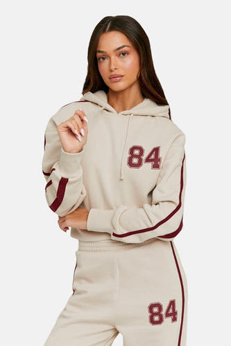 Gilet beige de TALLY WEIJL avec des rayures rouges foncées et le motif '84', porté avec un pantalon de jogging coordonné.