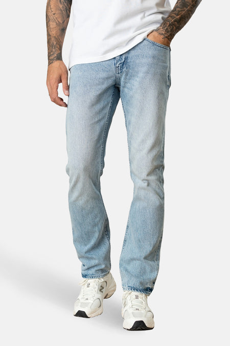 Rechte jeans in lichtblauw denim van Petrol Industries, met witte sneakers en zichtbare tatoeages.
