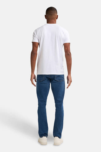 Rechte jeans in midblauw denim van Petrol Industries, met stiksels op de achterzakken, gecombineerd met een wit T-shirt en crèmekleurige schoenen, gezien van achteren.
