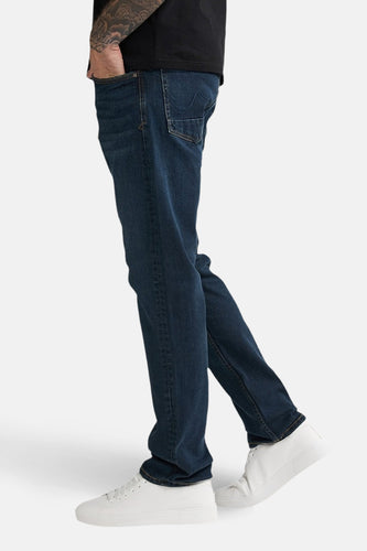 Donkerblauwe rechte jeans van Petrol Industries, gedragen met witte sneakers, in zijaanzicht.