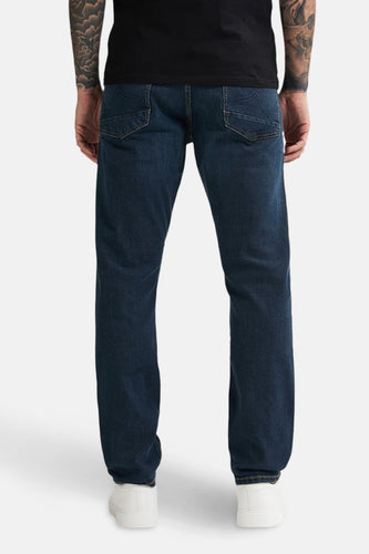 Donkerblauwe straight jeans van Petrol Industries, gezien vanaf de achterkant, met witte sneakers en tatoeages op de armen.