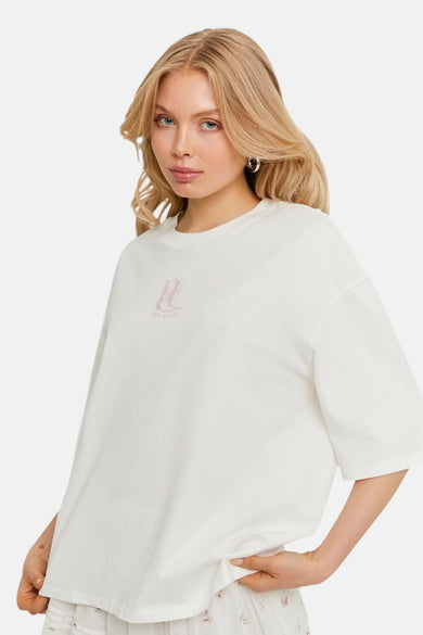 T-shirt blanc oversize de TALLY WEIJL avec imprimé bottes roses sur la poitrine, porté par une femme blonde.