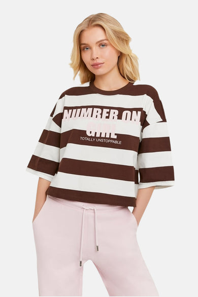 T-shirt rayé marron et blanc de TALLY WEIJL avec texte rose 'NUMBER ONE GIRL TOTALLY UNSTOPPABLE', porté avec un jogging rose.