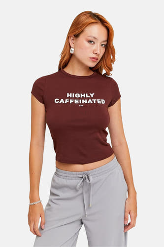 Bruin T-shirt met korte mouwen van TALLY WEIJL, met de tekst "Highly Caffeinated" en gecombineerd met een grijze joggingbroek.
