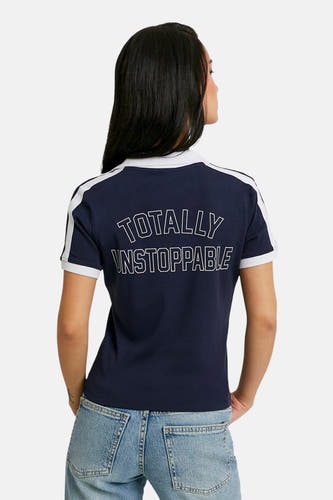 Polo bleu à manches courtes de TALLY WEIJL, avec des rayures blanches et "TOTALLY UNSTOPPABLE" dans le dos, porté avec un jean.