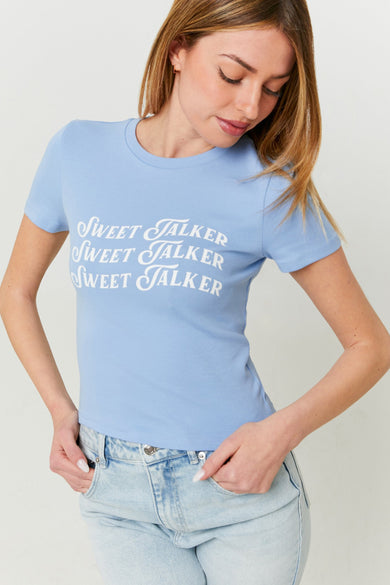 Blauw T-shirt met korte mouwen van TALLY WEIJL, met witte "Sweet Talker" tekstprint, gedragen met een spijkerbroek.
