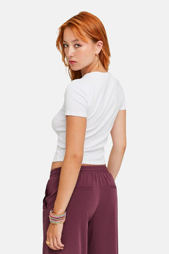T-shirt blanc à manches courtes de TALLY WEIJL, porté avec un pantalon bordeaux et des bracelets colorés.