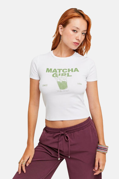 T-shirt blanc à manches courtes de TALLY WEIJL, avec une impression verte et porté avec un pantalon de jogging violet.