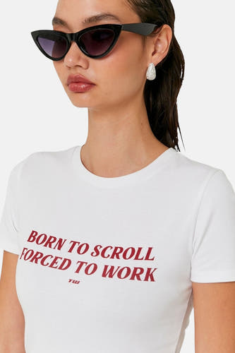 T-shirt blanc à manches courtes de TALLY WEIJL, avec une impression de texte rouge et porté avec un chapeau de soleil noir et des boucles d'oreilles argentées.
