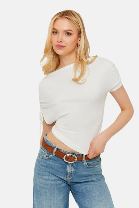 Witte korte mouwen t-shirt van TALLY WEIJL, asymmetrisch ontwerp met knoopdetail, gedragen met blauwe jeans en bruine riem, zijprofiel.